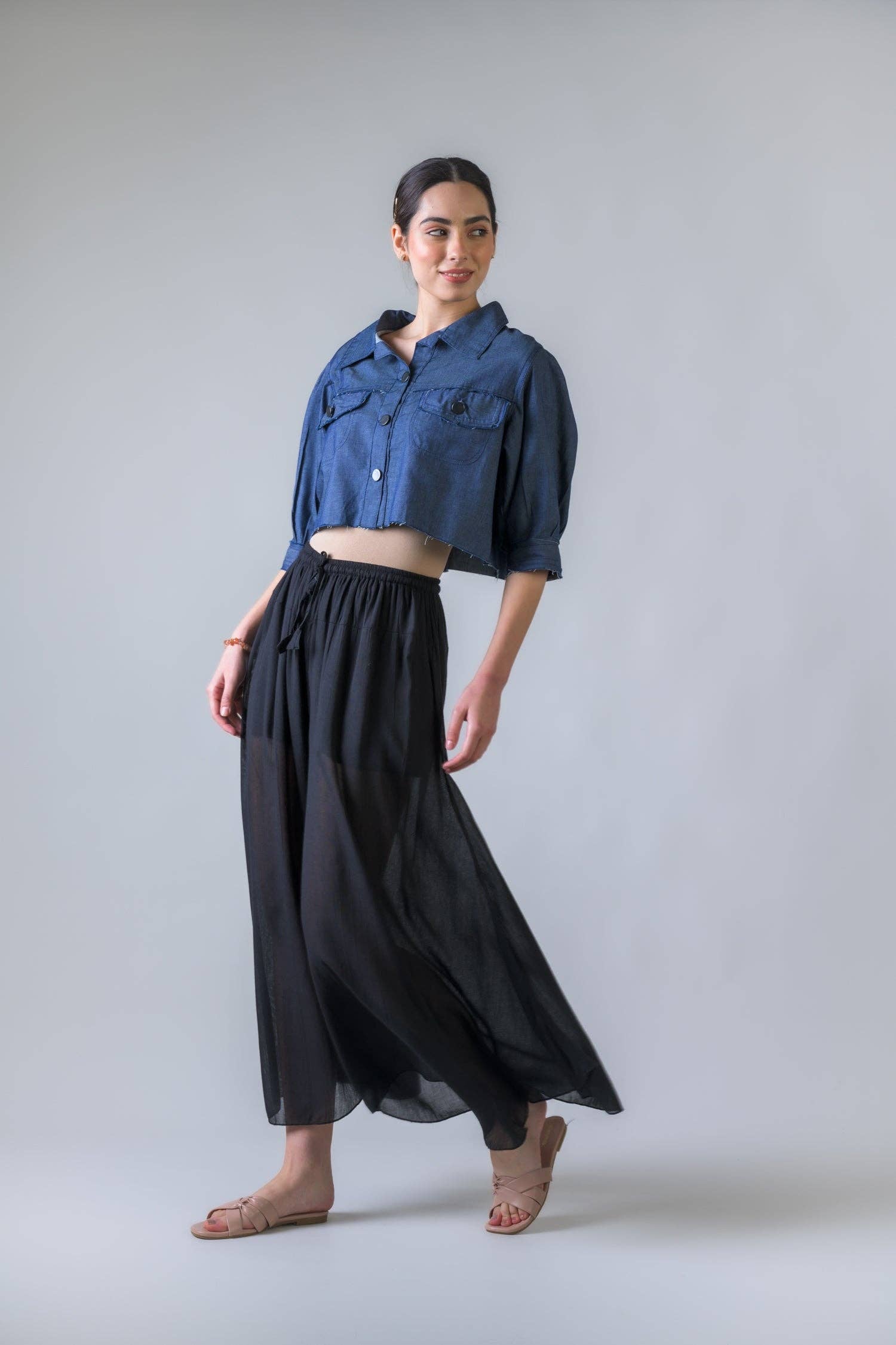 Woman wearing a blue denim shirt and black wide-leg pants on a plain background