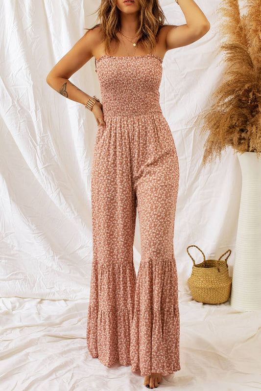 Woman wearing a pink floral jumpsuit against a white background with a woven basket and dried plants.