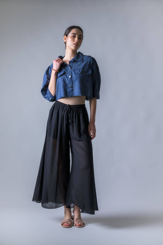 Woman wearing a blue denim shirt and black wide-leg pants against a gray background