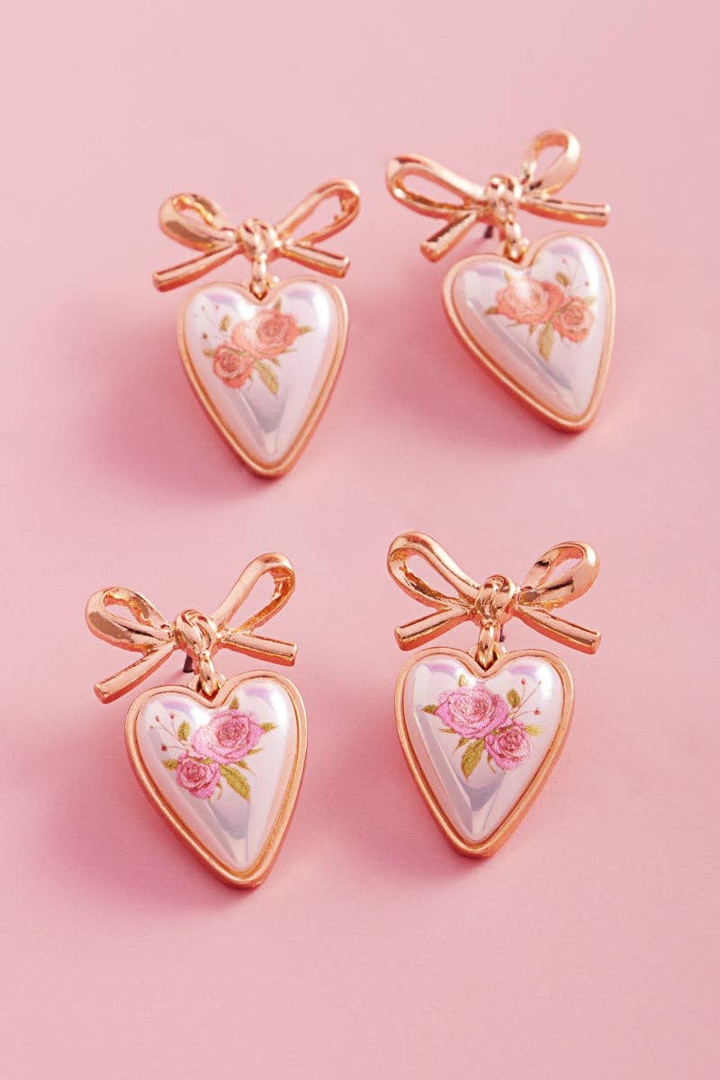 Heart-shaped earrings with floral designs and rose gold bows on a pink background