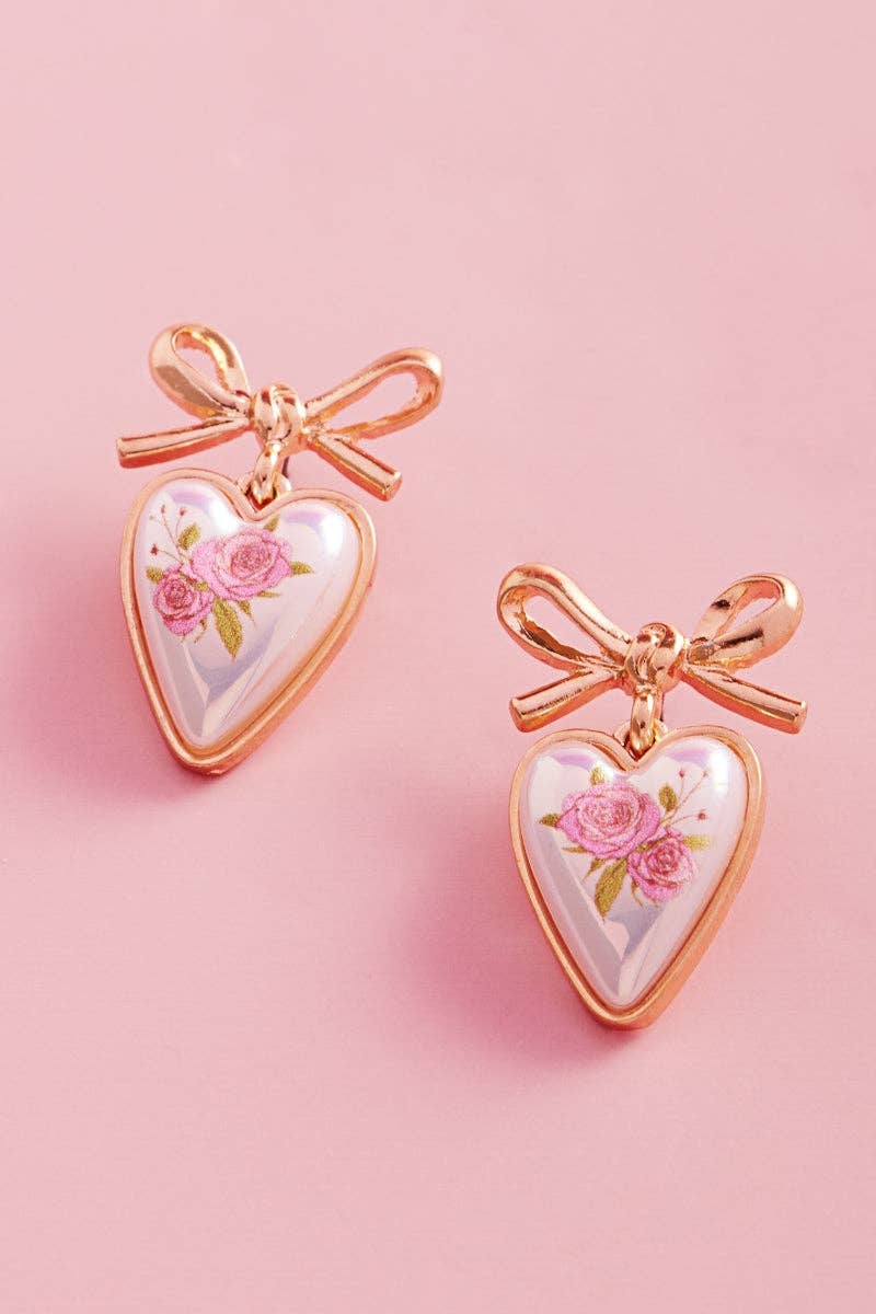 Heart-shaped earrings with floral design and rose gold bows on a pink background
