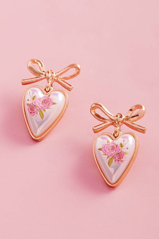 Heart-shaped earrings with floral design and rose gold bows on a pink background