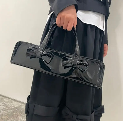 Black glossy baguette handbag by essecoco featuring double bow detail and compact, stylish design.