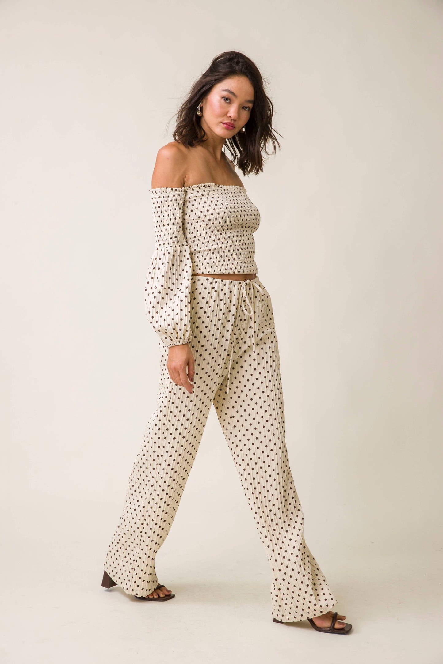 Woman wearing a polka dot outfit with long sleeves and pants on a plain background
