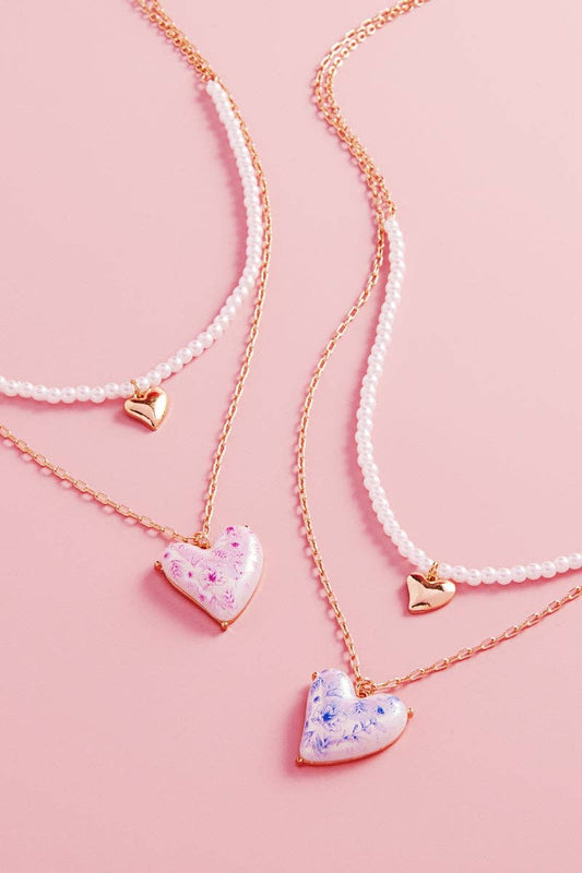Two pearl necklaces with heart-shaped pendants on a pink background
