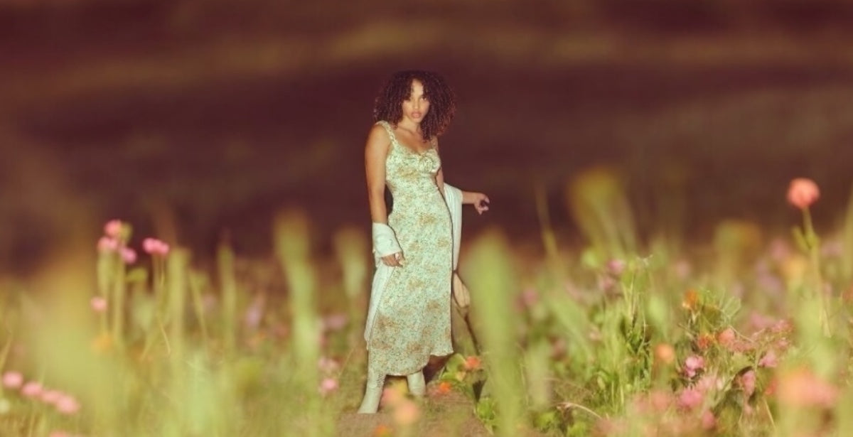 Woman in a floral dress standing in a field of flowers with a blurred background
